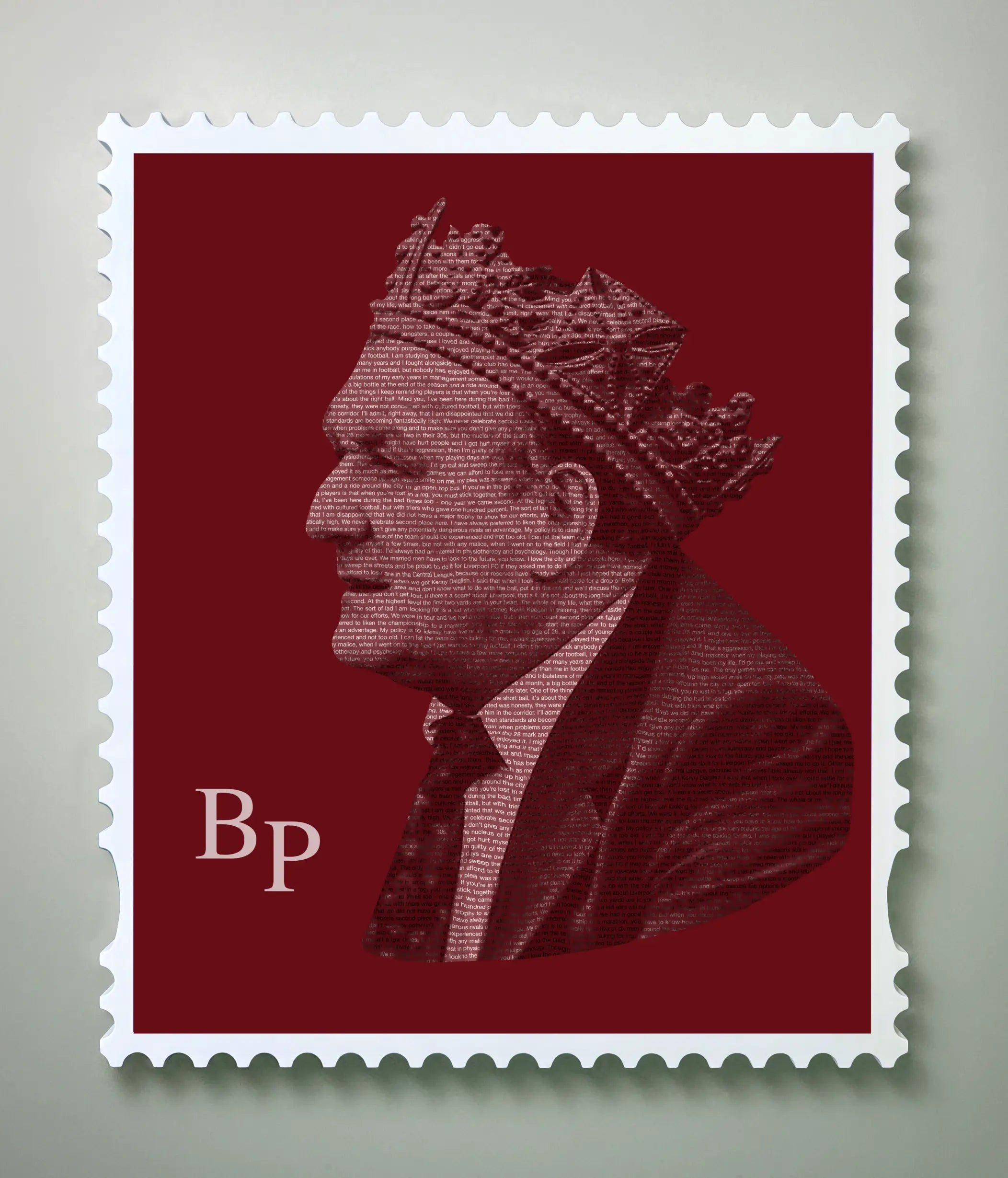 Front-on view of the Bob Paisley typography stamp artwork in a handmade white wooden stamp frame against a light grey background. The crimson portrait – built entirely from Bob Paisley's own words in fine typography – shows him in profile wearing a crown. The floating frame casts a subtle shadow, highlighting the depth and premium finish of the gallery-grade aluminium dibond print.