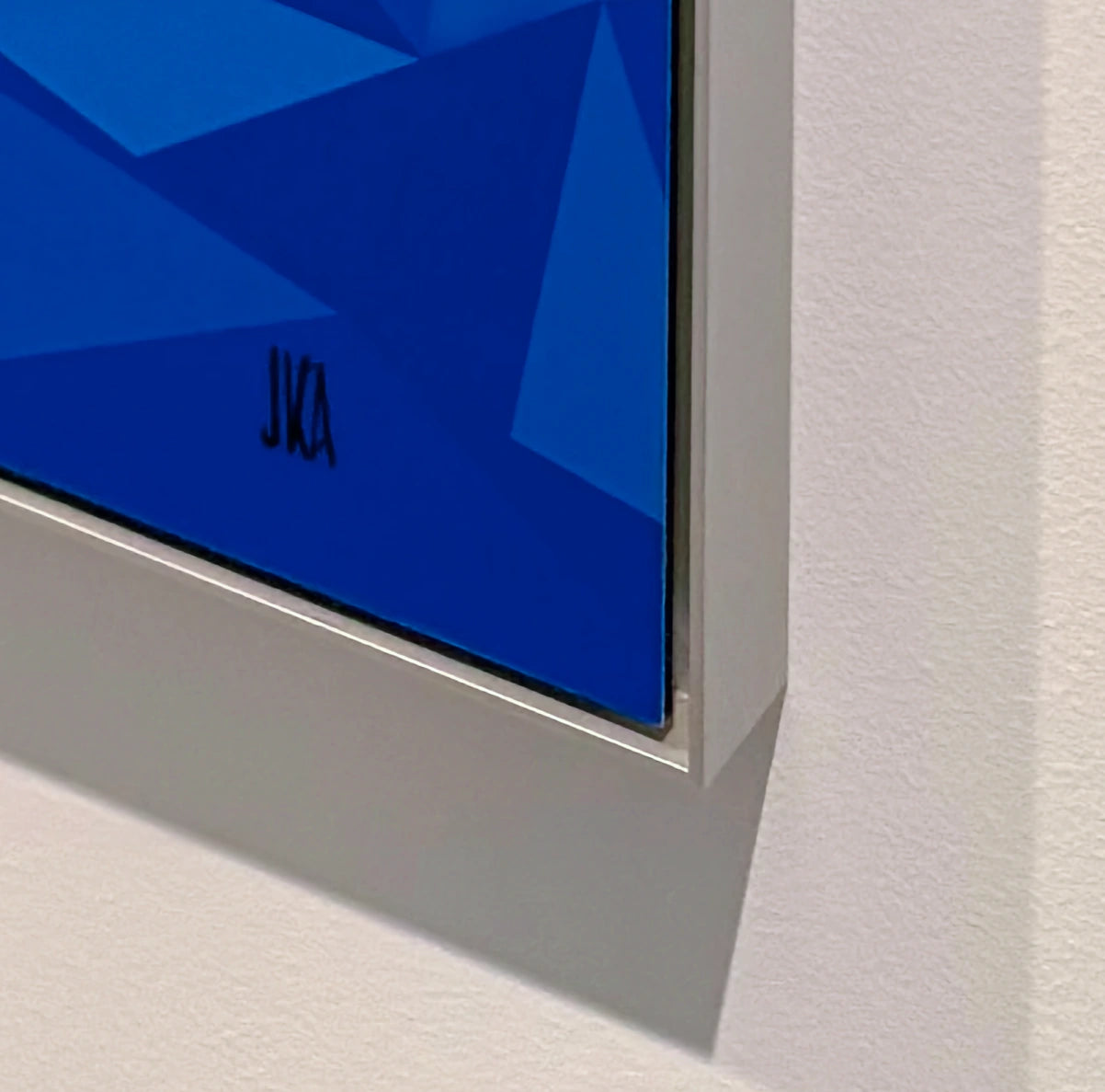 Close-up of the lower corner of the geometric Little Mermaid aluminium dibond print, showing the original artist's initials and silver floater frame against a white wall.