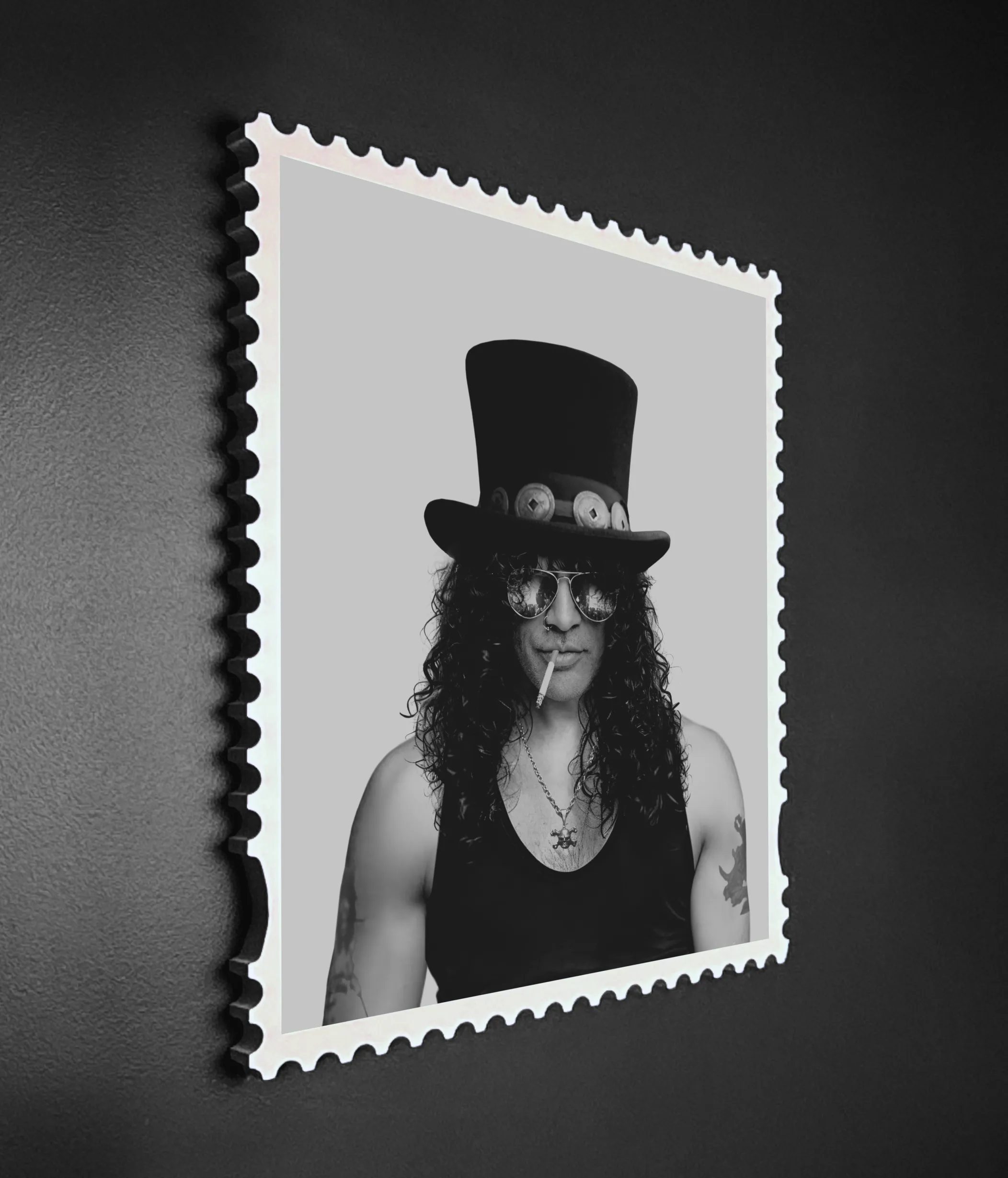 Angled wall-mounted view of the Slash Skin & Bones lenticular artwork showing the portrait state – black and white photograph in a postage stamp frame mounted on a dark textured wall.